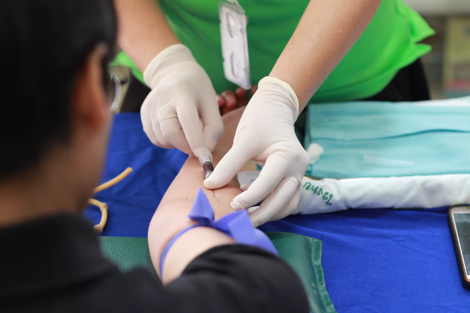 Profissional com luvas coleta sangue do braço de uma pessoa