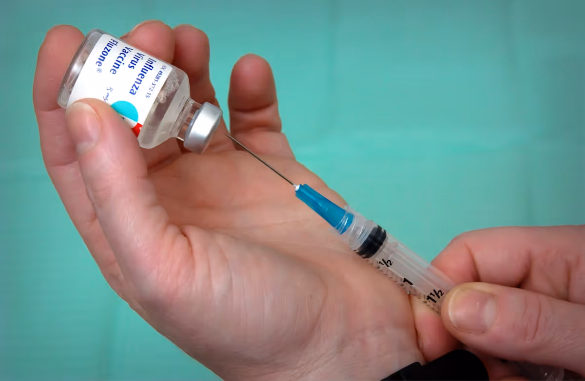 Mão enluvada retirando dose de vacina com seringa de frasco