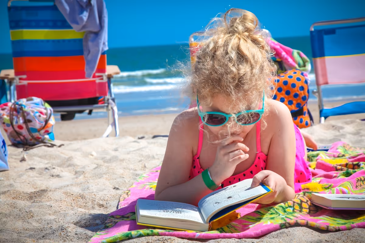 Criança com óculos de sol lendo livro na praia ao sol Criança com óculos de sol lendo livro na praia ao sol