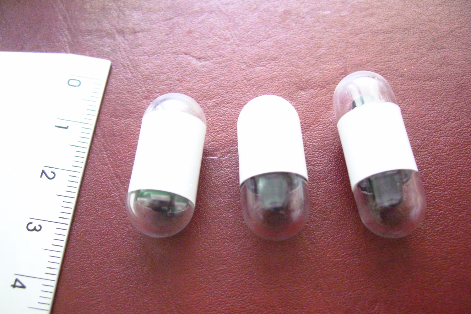 Três cápsulas endoscópicas ao lado de uma régua Três cápsulas endoscópicas ao lado de uma régua