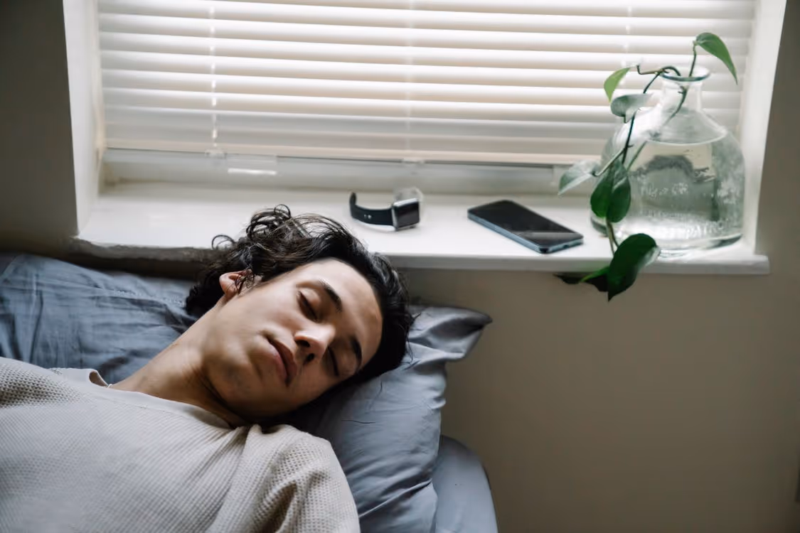 Jovem dormindo em cama com smartwatch e celular sobre a janela ao lado Jovem dormindo em cama com smartwatch e celular sobre a janela ao lado