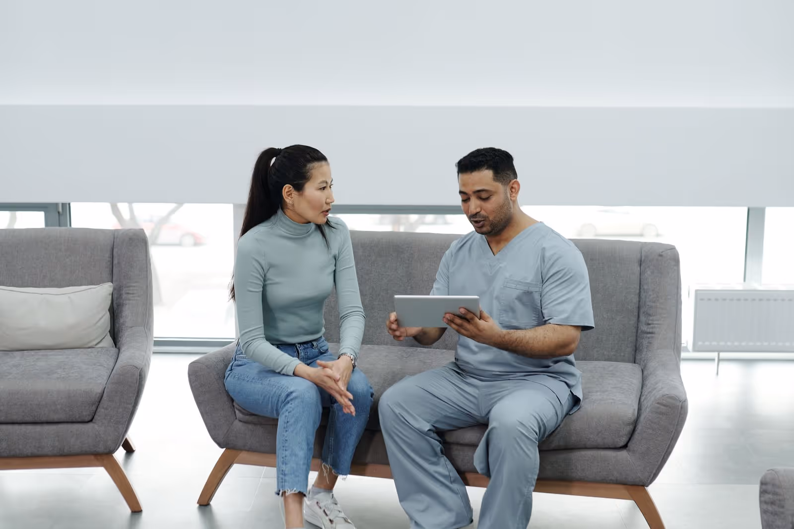 Profissional de saúde mostra informações em um tablet a uma paciente sentada em uma clínica Profissional de saúde mostra informações em um tablet a uma paciente sentada em uma clínica