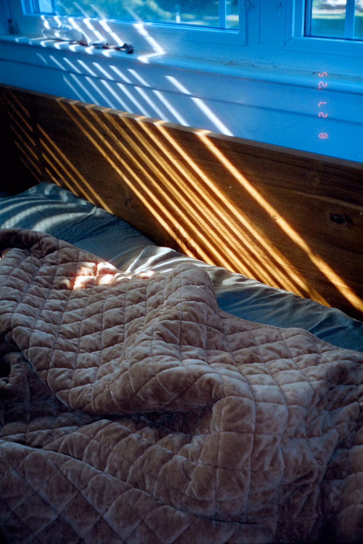 Listras de luz do sol filtradas por persiana sobre cama desfeita
