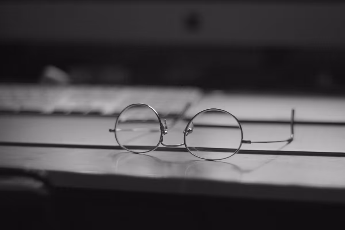 Óculos sobre teclado em luz baixa, evocando trabalho prolongado em frente à tela