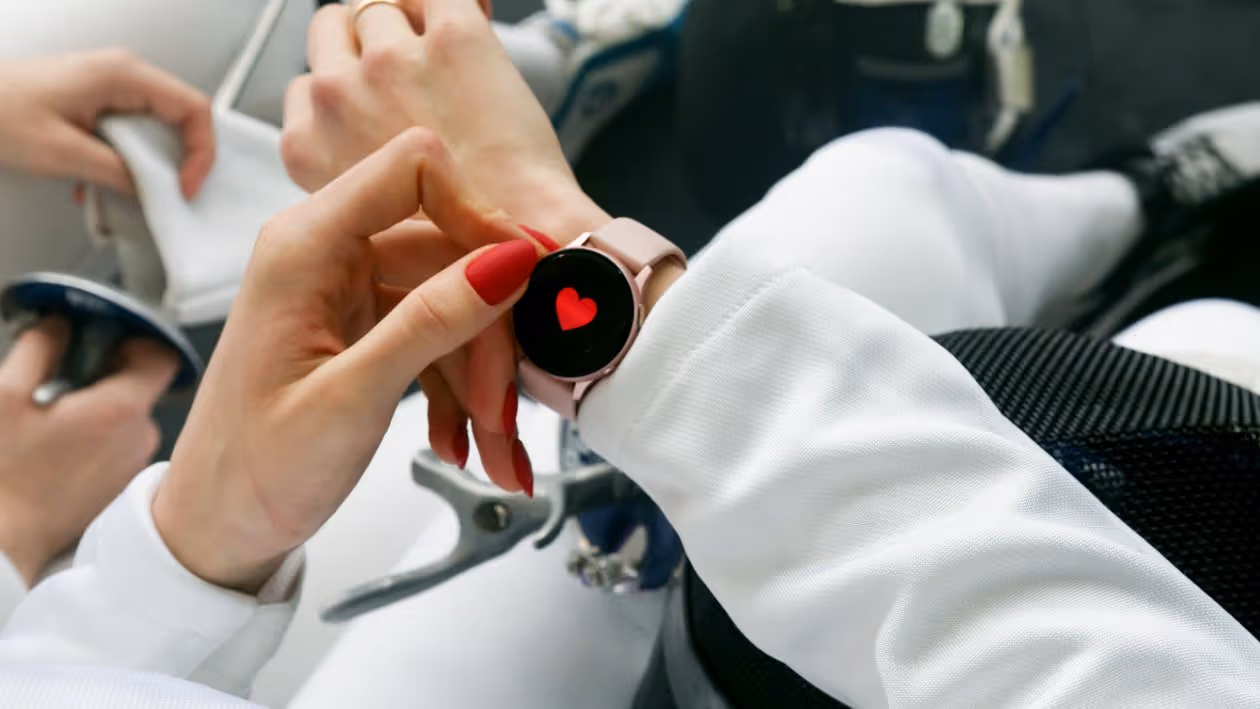 Mão de mulher com unhas vermelhas interagindo com smartwatch que exibe ícone de coração Mão de mulher com unhas vermelhas interagindo com smartwatch que exibe ícone de coração